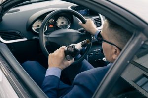 man in an expensive suit drinks beer at the wheel of a car causing the danger of an emergency. A businessman drinks while driving. Drunk driver concept