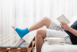 Man with a broken leg in a cast sits at home and reads books.