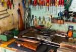 Workplace of gunsmith in professional weapons workshop with tools and disassembled shotgun during repair or maintenance