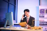Young lawyer at desk with legal scales and gavel, writing documents in office, offering legal services