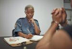 Security, criminal and female police officer at the station writing a legal report for social justice. Law enforcement, crime and male thief in handcuffs talking to woman guard in interrogation room.