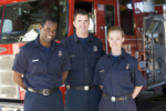Portrait of three firefighters standing by a fire engine