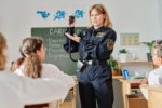 Caucasian policewoman standing in classroom demonstrating transmitter device to group of students during vocational guidance class