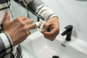 Anonymous Young Man Removing Adhesive from Injured Finger with Stack Splint. A person removing carefully the adhesive bandage from an injured finger in the bathroom.