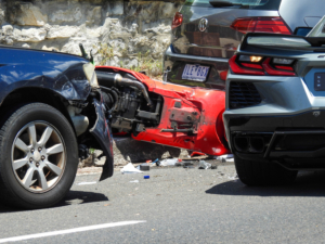 Damaged cars and a scooter involved in a traffic accident on Bondi Road near Bondi Beach. The hazard lights of the Chevrolet Corvette (right) are flashing. The scooter on the ground is a Vespa. The other cars are Subaru and Volkswagen. The road was closed in both directions for several hours. This image was taken near the corner of Dudley Street and Bondi Road on a sunny afternoon on 26 November 2023.
