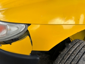 yellow car with visible cosmetic damage to the front bumper and fender area, from a collision