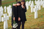 Holds flowers. Two young women in black clothes visiting cemetery with many white crosses. Conception of funeral and death