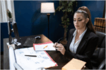 professional woman in a black blazer reading documents at her office desk