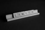 Scrabble tiles arranged on a rack to spell the word "LAWYER"
