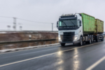 White truck hauls a container trailer on a slick winter road with dramatic motion blur and gray sky. Strong fit for intermodal freight, globaltrade and supplychain concepts.