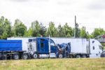 Accidentally broken down while driving blue big rig semi truck with open hood and loaded flat bed semi trailer stands on the highway shoulder waiting for mobile repair service