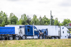 Accidentally broken down while driving blue big rig semi truck with open hood and loaded flat bed semi trailer stands on the highway shoulder waiting for mobile repair service