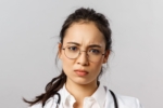 Person in a white lab coat with a stethoscope draped around their neck, wearing circular spectacles