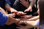 Diverse group of people placing their hands together in a circle, a common gesture representing unity