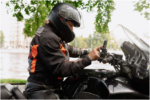 wearing a dark protective helmet and riding gear while adjusting controls on the handlebars of a motorcycle