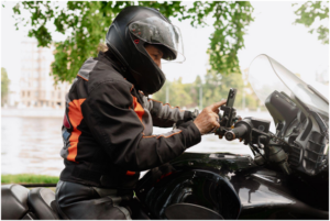 wearing a dark protective helmet and riding gear while adjusting controls on the handlebars of a motorcycle