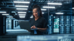 Portrait of Multiracial Mature Female IT Specialist Using Laptop, Standing in Data Center. Infrastructure Architect Works on Web Services. Cloud Computing, Server Analytics, Cyber Security Maintenance