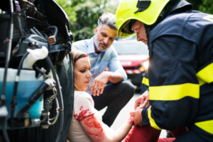 A firefighter helping a young injured woman sitting by the car on a road after an accident, unconscious.