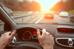 Driving on highway road, closeup hands of car driver on steering wheel, road trip at sunset