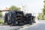 A view of the rear wheels of a overturned truck on a small street in an accident.
