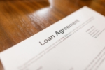 A close-up of a printed paper document with the words "Loan Agreement" at the top resting on a wooden surface