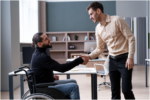 person in a wheelchair shaking hands with a standing colleague in an office setting