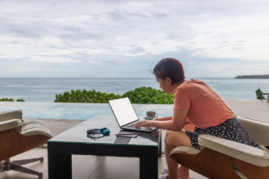 Happy working senior digital nomad woman sitting with laptop at luxury pool villa near beach, Phuket Thailand.