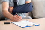 Close up of a man hands with broken arm signing insurance document after car accident at home