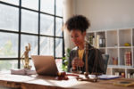 African American female lawyer consulting a client via video conference from a modern office with justice symbols, providing legal advice and reviewing documents remotely