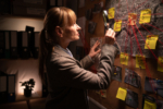 Woman detective by evidence board studying leads for investigation and criminal case working in office at night . Female Investigator problem solving with crime analysis.