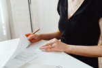 Woman in a black top examining and signing documents at a white desk